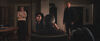 Bilde fra filmen "Gjensyn" hvor vi i forgrunnen ser en mann bakfra sittende i en stol i en mørk stue og familien står rundt og ser alvorlig og skeptisk på ham.