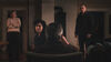 Bilde fra filmen "Gjensyn" hvor vi i forgrunnen ser en mann bakfra sittende i en stol i en mørk stue og familien står rundt og ser alvorlig og skeptisk på ham.